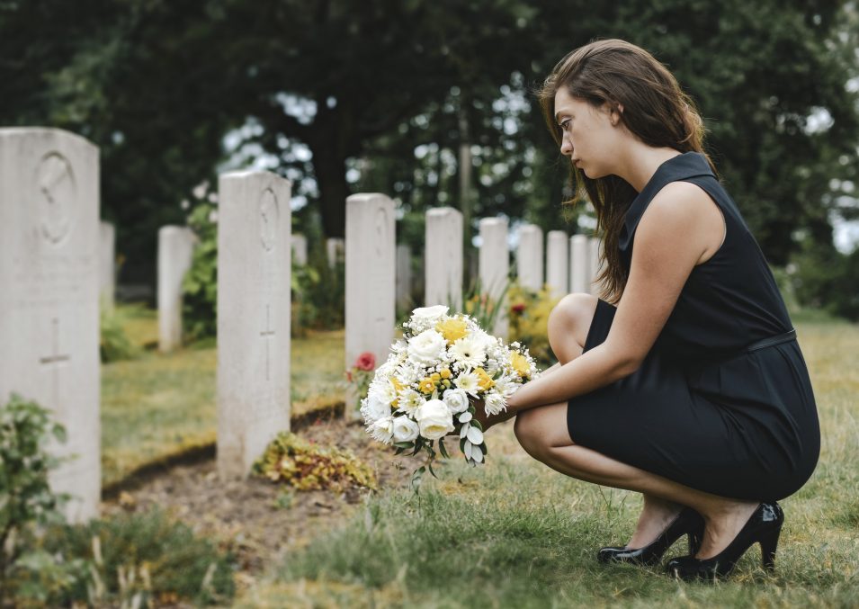 Young widow laying flowers at the grave